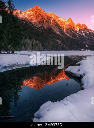 Les montagnes enneigées des Alpes reflétaient des couleurs chaudes dans le lac partiellement gelé d'Anterselva (Italie du Nord) au coucher du soleil en hiver. Neige et glace à l'avant Banque D'Images