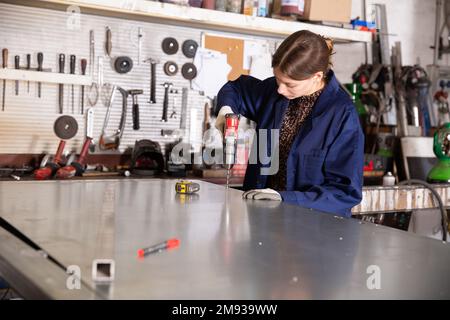 Femme travaillant avec des tôles et utilisant une perceuse électrique Banque D'Images