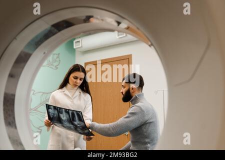 Le radiologue d'acquisition CT montre les rayons X de l'abdomen au patient dans la salle d'acquisition calculée. CT médecin consultant le patient et montrant les rayons X de la poitrine au patient Banque D'Images