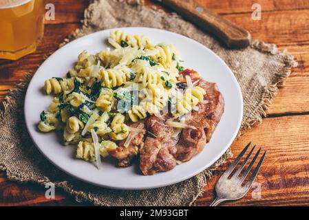 Steak de porc et pâtes crémeuses aux épinards et au thym Garni de parmesan râpé sur plaque blanche Banque D'Images