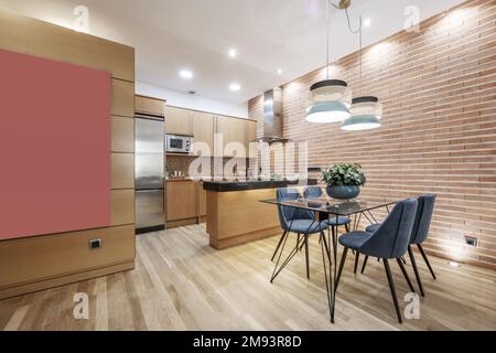 Cet appartement studio comprend une cuisine ouverte avec comptoirs en granit noir poli, un mur en briques, une table à manger en verre avec chaises bleues et des planchers de bois franc en chêne Banque D'Images