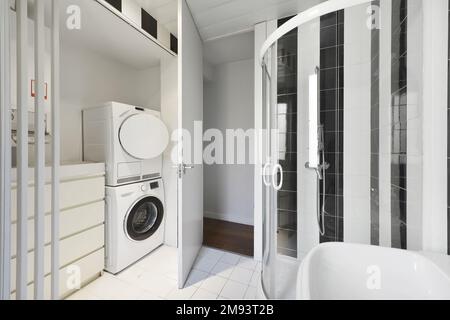 Salle de bains avec armoires blanches, cabine de douche vitrée, laveuse et sécheuse blanches Banque D'Images