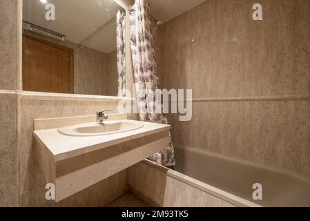 Salle de bains carrelée en marbre crème avec miroir intégré, bordures et toilettes en marbre et baignoire en porcelaine avec rideaux Banque D'Images