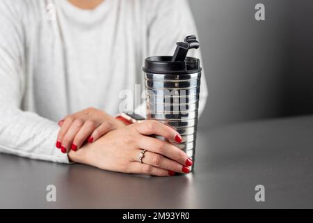 Femme avec un thermos en aluminium dans ses mains, tout en se reposant à une table. Banque D'Images
