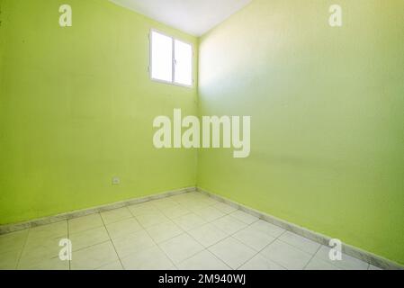 Chambre vide avec murs peints vert pistache avec sol carrelé blanc et une fenêtre en aluminium dans un coin Banque D'Images