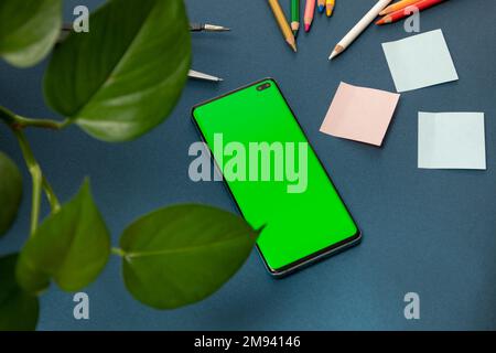 téléphone cellulaire avec écran vert pour mettre de la publicité, sur un bureau avec des fournitures de bureau Banque D'Images