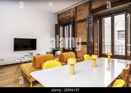 Salon d'un appartement de vacances avec un mur d'époque avec de grands balcons avec des volets en bois marron et des meubles modernes de design avec jaune Banque D'Images