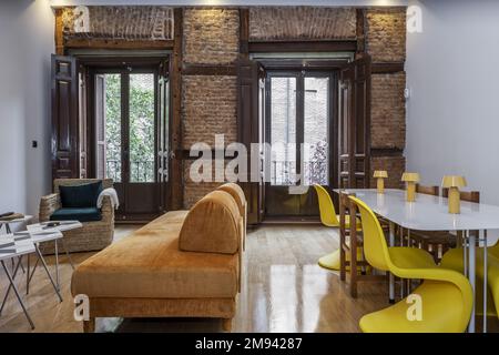 Séjour avec mur en briques vintage avec poutres en bois et en métal, volets en bois marron et détails décoratifs jaunes Banque D'Images