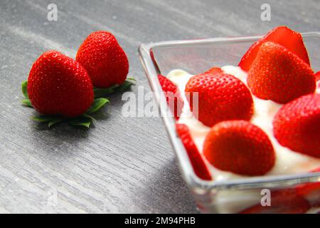 Dessert sucré, fraises rouges aux fruits en verre réfractaires à la crème et au yaourt sur fond de bois gris vintage Banque D'Images