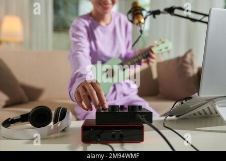 Gros plan de l'adolescente qui monte le volume sur l'amplificateur lors de l'enregistrement elle-même jouant ukulele Banque D'Images