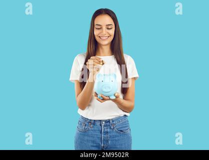 Portrait de la femme heureuse qui met la pièce dans la banque de piggy, économiser de l'argent pour l'achat qu'elle rêve de. Banque D'Images