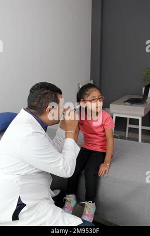 Médecin pédiatre professionnel et patient jeune fille à poil brun Latino de 4 ans sont en consultation pour vérifier leurs yeux, leur bouche et leur gorge Banque D'Images