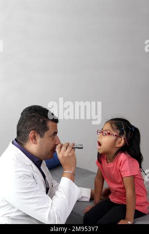 Médecin pédiatre professionnel et patient jeune fille à poil brun Latino de 4 ans sont en consultation pour vérifier leurs yeux, leur bouche et leur gorge Banque D'Images