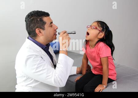 Médecin pédiatre professionnel et patient jeune fille à poil brun Latino de 4 ans sont en consultation pour vérifier leurs yeux, leur bouche et leur gorge Banque D'Images