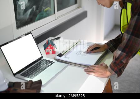 Photo rognée d'un ingénieur travaillant avec des plans et vérifiant le calendrier sur son ordinateur portable Banque D'Images