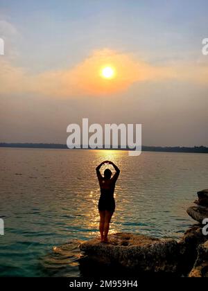 Une jeune femme avec yoga pose au coucher du soleil au bord d'un beau lac de Lachua, Alta Verapaz, Guatemala Banque D'Images