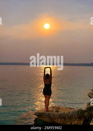 Une jeune femme avec yoga pose au coucher du soleil au bord d'un beau lac de Lachua, Alta Verapaz, Guatemala Banque D'Images