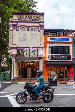 Homme sur moto pass tissu et magasins de textile dans les shophouses traditionnelles sur Arab St Kampong Glam Singapour Banque D'Images