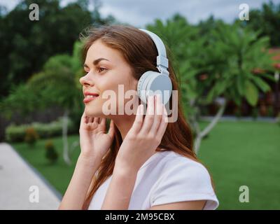 Portrait de femme en casque bonheur sourire dans un T-shirt blanc écouter de la musique et marcher dans la rue, devant les palmiers Banque D'Images