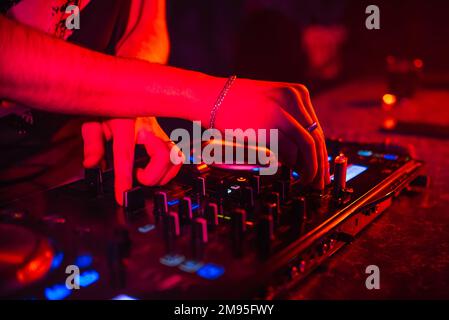 Mains du DJ sur le mélangeur jouant de la musique en boîte de nuit sur la fête avec éclairage rouge Banque D'Images