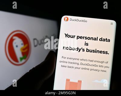 Personne tenant un smartphone avec la page Web du moteur de recherche Internet DuckDuckGo (DDG) à l'écran devant le logo. Concentrez-vous sur le centre de l'écran du téléphone. Banque D'Images