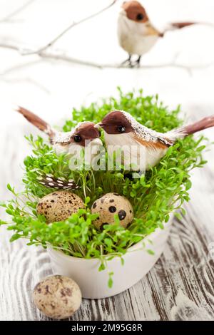 Décoration de table de Pâques : oiseaux décoratifs et œufs d'équidés sur la salade de cresson fraîche dans un plat blanc. Banque D'Images