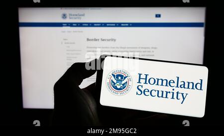 Personne tenant un smartphone portant le sceau du département américain de la sécurité intérieure (DHS) à l'écran devant le site Web. Mise au point sur l'affichage du téléphone. Banque D'Images