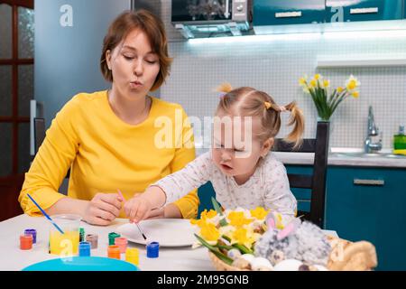 Fête de Pâques. Mère et sa petite fille peignant des œufs. Petite fille ayant du plaisir et des peintures sur l'assiette. Banque D'Images