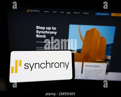 Personne détenant un smartphone avec le logo de la société américaine de services financiers synchrony Bank sur l'écran devant le site Web. Mise au point sur l'affichage du téléphone. Banque D'Images