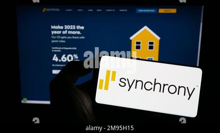 Personne tenant un téléphone portable avec le logo de la société américaine de services financiers synchrony Bank à l'écran en face de la page Web. Mise au point sur l'affichage du téléphone. Banque D'Images
