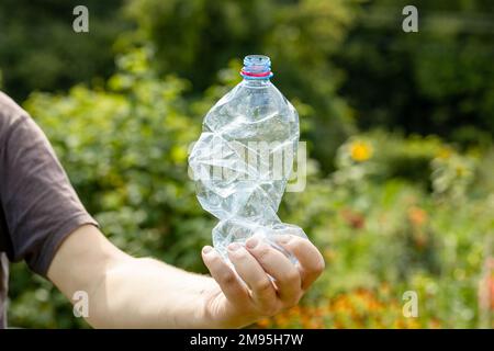 Main tenant une bouteille en plastique vide froissés dans le parc Banque D'Images