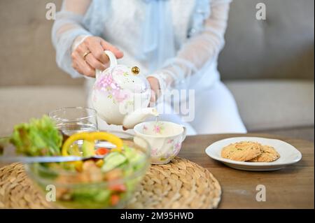 Charmante femme asiatique agée de thé chaud de belle théière vintage dans une tasse, aime prendre le thé de l'après-midi dans le salon. rogné et gros plan i Banque D'Images