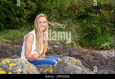 Rhianna Martin, une belle femme blonde, est assise sur des rochers tout en ayant sa photo prise à la plage de Wormit, dans le comté de Fife, en Écosse, au Royaume-Uni Banque D'Images