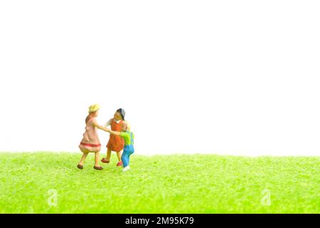 Photographie miniature de personnage de jouet de personnes. Concept d'arène de jeux. Les enfants jouent ensemble au-dessus de l'herbe verte. Isolé sur fond blanc. Image Banque D'Images