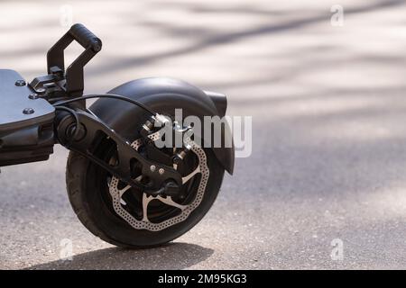 Aile arrière avec roue de scooter électrique sur fond d'asphalte par temps ensoleillé. Banque D'Images