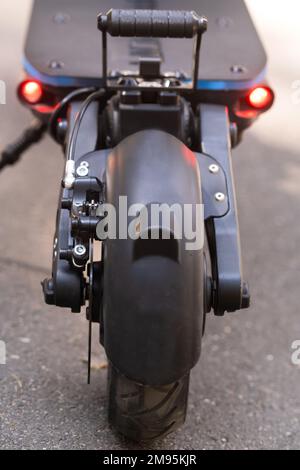 L'arrière du scooter électrique avec un pied repose sur le fond d'asphalte par temps ensoleillé. Banque D'Images