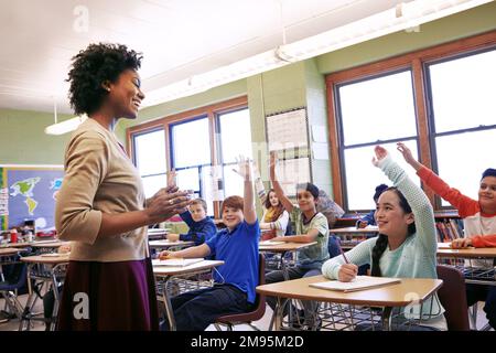L'école, l'enseignant et les enfants lèvent leurs mains pour poser ou répondre à une question académique pour l'apprentissage. Diversité, éducation et enfants de l'école primaire Banque D'Images