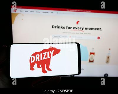 Personne tenant un smartphone avec le logo de la société américaine de livraison d'alcool Drizly LLC sur l'écran devant le site Web. Mise au point sur l'affichage du téléphone. Banque D'Images