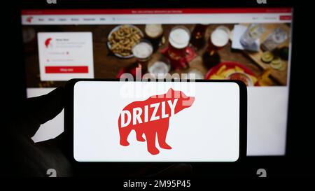 Personne tenant un téléphone portable avec le logo de la compagnie américaine de livraison d'alcool Drizly LLC sur l'écran en face de la page Web. Mise au point sur l'affichage du téléphone. Banque D'Images