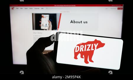 Personne tenant le téléphone portable avec le logo de la société américaine de livraison d'alcool Drizly LLC sur l'écran devant la page Web d'affaires. Mise au point sur l'affichage du téléphone. Banque D'Images