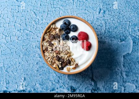 Yaourt avec baies et muesli pour le petit déjeuner dans un bol sur fond de lbue Banque D'Images