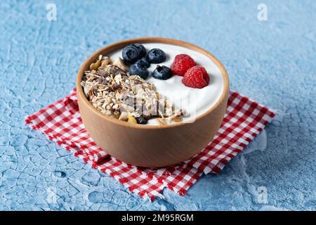 Yaourt avec baies et muesli pour le petit déjeuner dans un bol sur fond de lbue Banque D'Images
