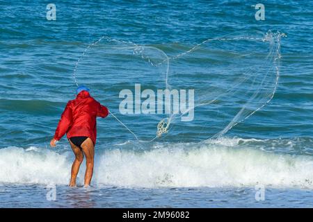 Homme jetant le filet de pêche de la plage à Porto Recanati, Puglia, Italie Banque D'Images