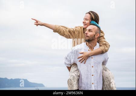 Un jeune couple marche sur une route entourée par la nature, avec l'homme portant la femme sur son dos Banque D'Images