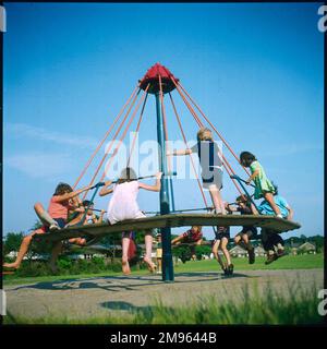 Enfants jouant sur un rond-point "parapluie" sur Lindfield Common, Sussex, Angleterre. Banque D'Images