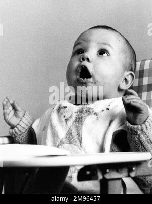 Un bébé assis dans une chaise haute regarde dans l'attente de la prochaine bouche de nourriture Banque D'Images