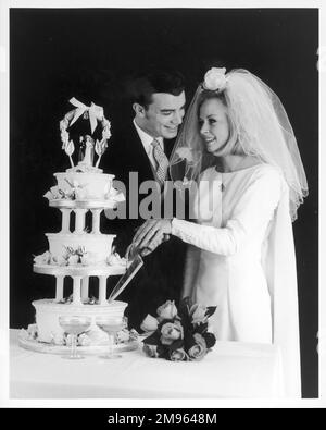 Les newlyweds posent pour l'appareil photo comme ils font la première coupe dans leur gâteau de mariage. Banque D'Images