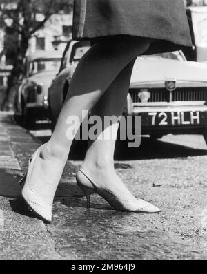 Une photo en gros plan des jambes d'une femme qui sortent d'un trottoir avec une paire de chaussures à talons hauts. Banque D'Images