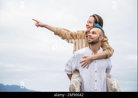 Un jeune couple marche sur une route entourée par la nature, avec l'homme portant la femme sur son dos Banque D'Images