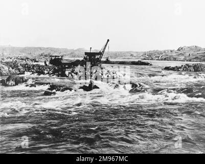 Construction du barrage d'Assouan (l'ancien barrage ou le barrage bas) sur le Nil en Égypte: Construction temporaire de la pierre et du sable dans le chenal central. Banque D'Images